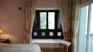 Ein Zimmer mit einem Bett, einem Sessel, einem Fenster mit Blick und einer Lampe.