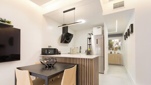 A modern kitchen with a central island, a dining area with a black table and wooden chairs, and a flat-screen TV mounted on the wall. - Magic Stay in Granada With Private Parking (Granada)