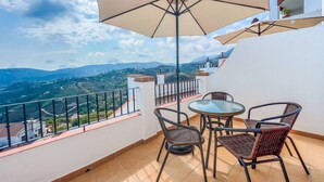 Un balcon avec une table et des chaises, un grand parasol et une vue panoramique sur la campagne.