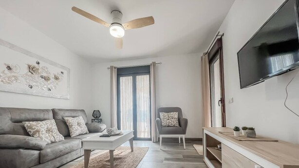 Un salon moderne avec un canapé gris, une table basse, un téléviseur fixé au mur et un ventilateur de plafond.