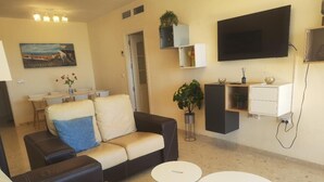 A living room with a sofa, two round coffee tables, a flat-screen TV, and a dining area with a table and chairs.