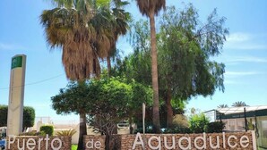 A sign with "Puerto de Aguadulce" written on it, surrounded by palm trees and a clear sky.