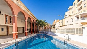 A swimming pool with a clear blue water, surrounded by buildings with arched walkways and balconies.