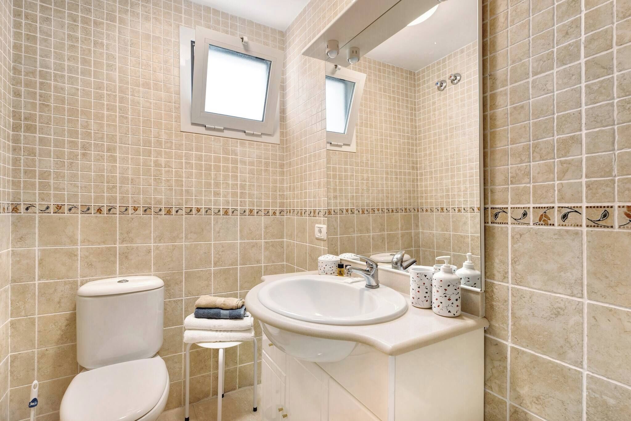 Une salle de bain avec des murs carrelés de couleur beige, un lavabo blanc et des toilettes.