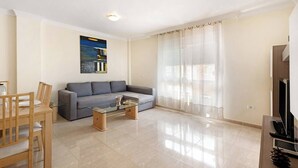 A modern living room with a grey sofa, a glass coffee table, and a wooden dining set. - Las Brisas Playa San Juan (Guia de Isora)