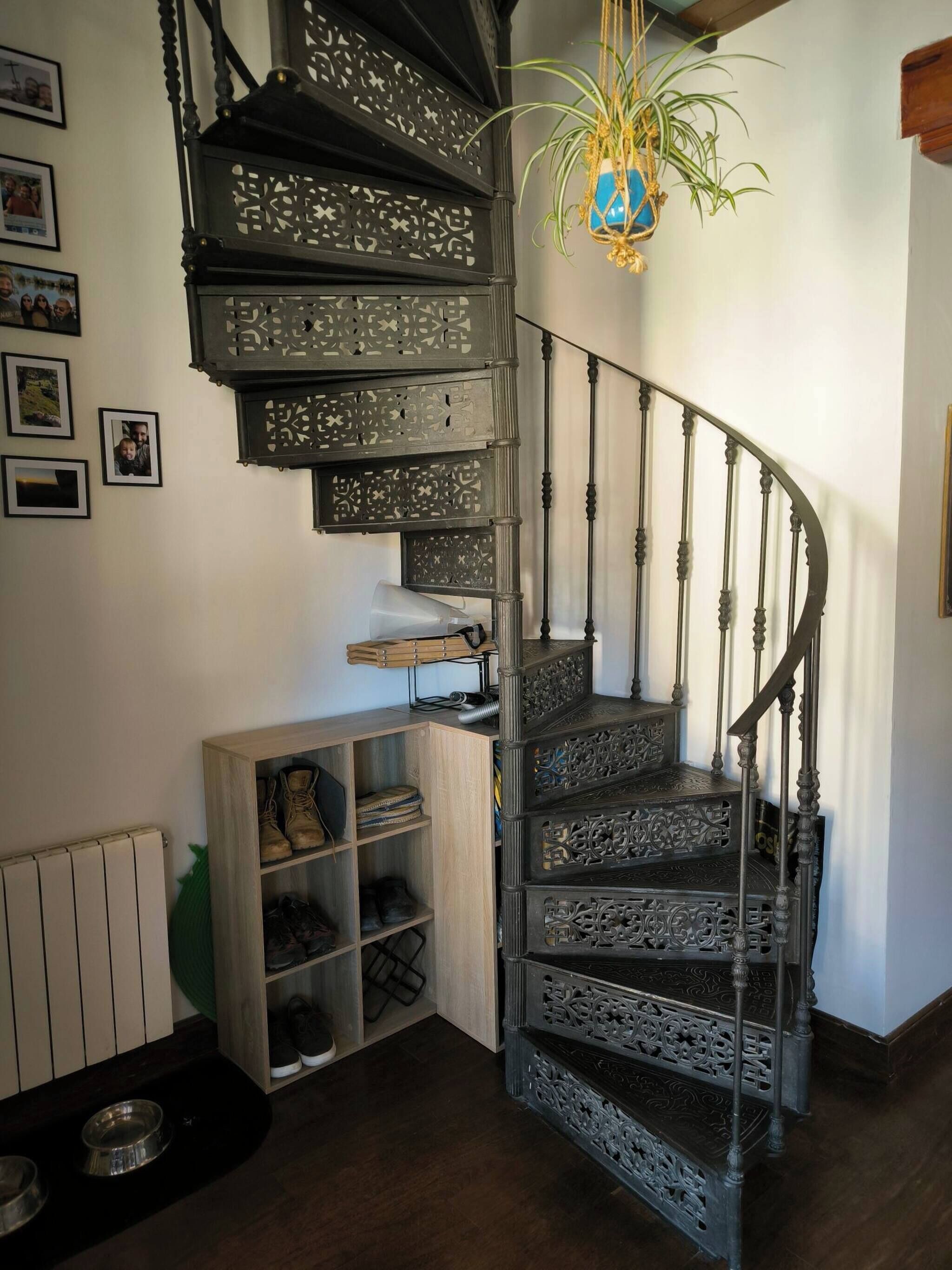 A spiral staircase with ornate metal railings and a wooden shoe rack beside it.