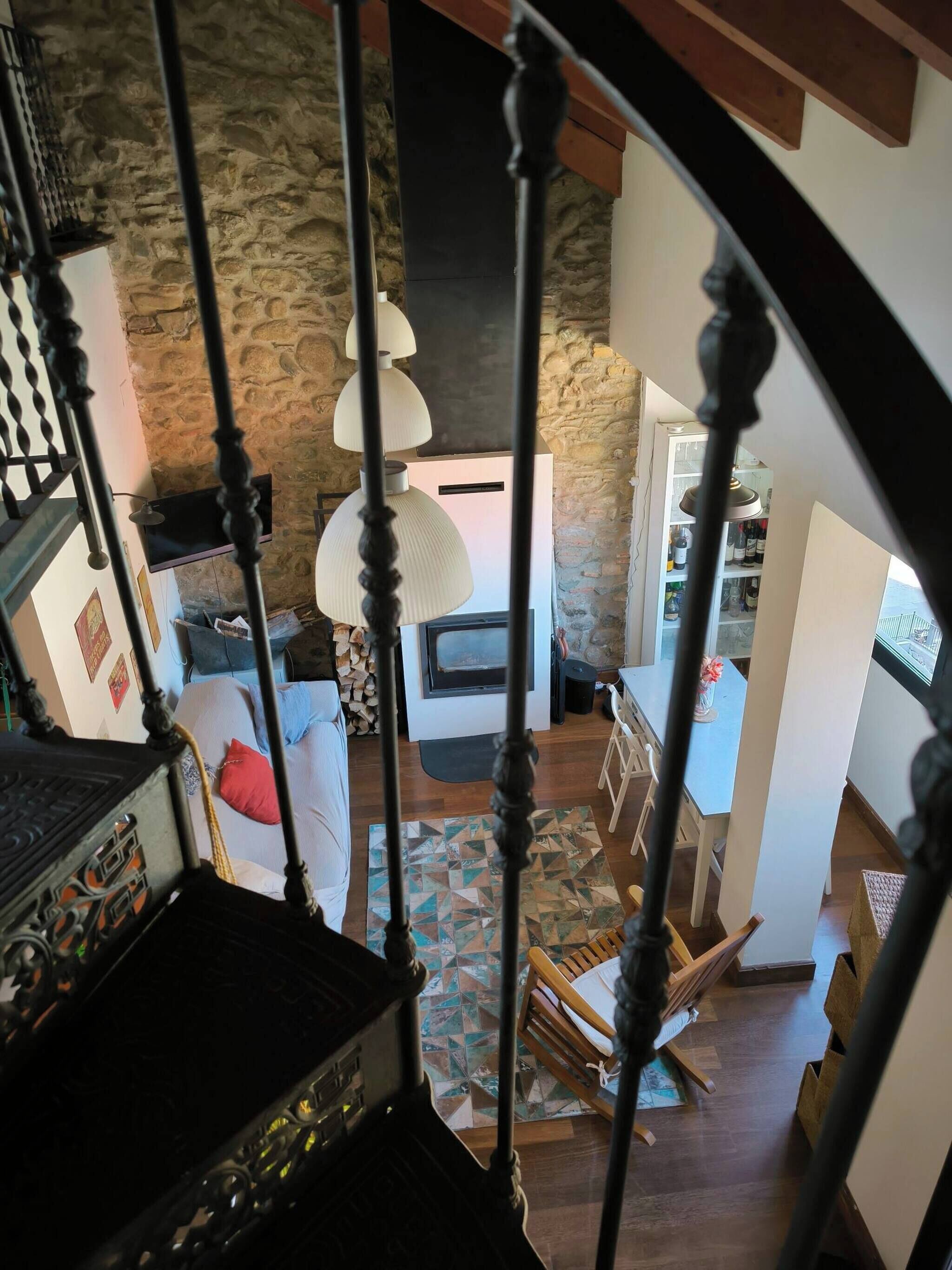 A staircase with ornate balusters leading to a living area with a stone wall, a fireplace, and a dining area with a table and chairs.