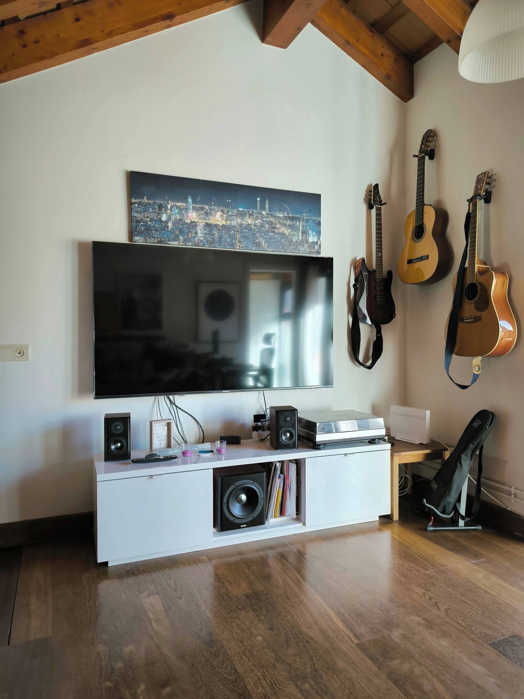 A modern living room with a flat-screen TV, a white entertainment unit, and acoustic guitars on the wall.