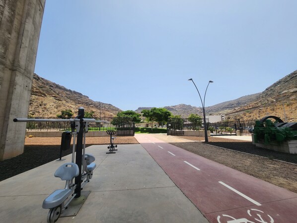 A paved path with exercise equipment, a red bike lane, and a mountainous backdrop.