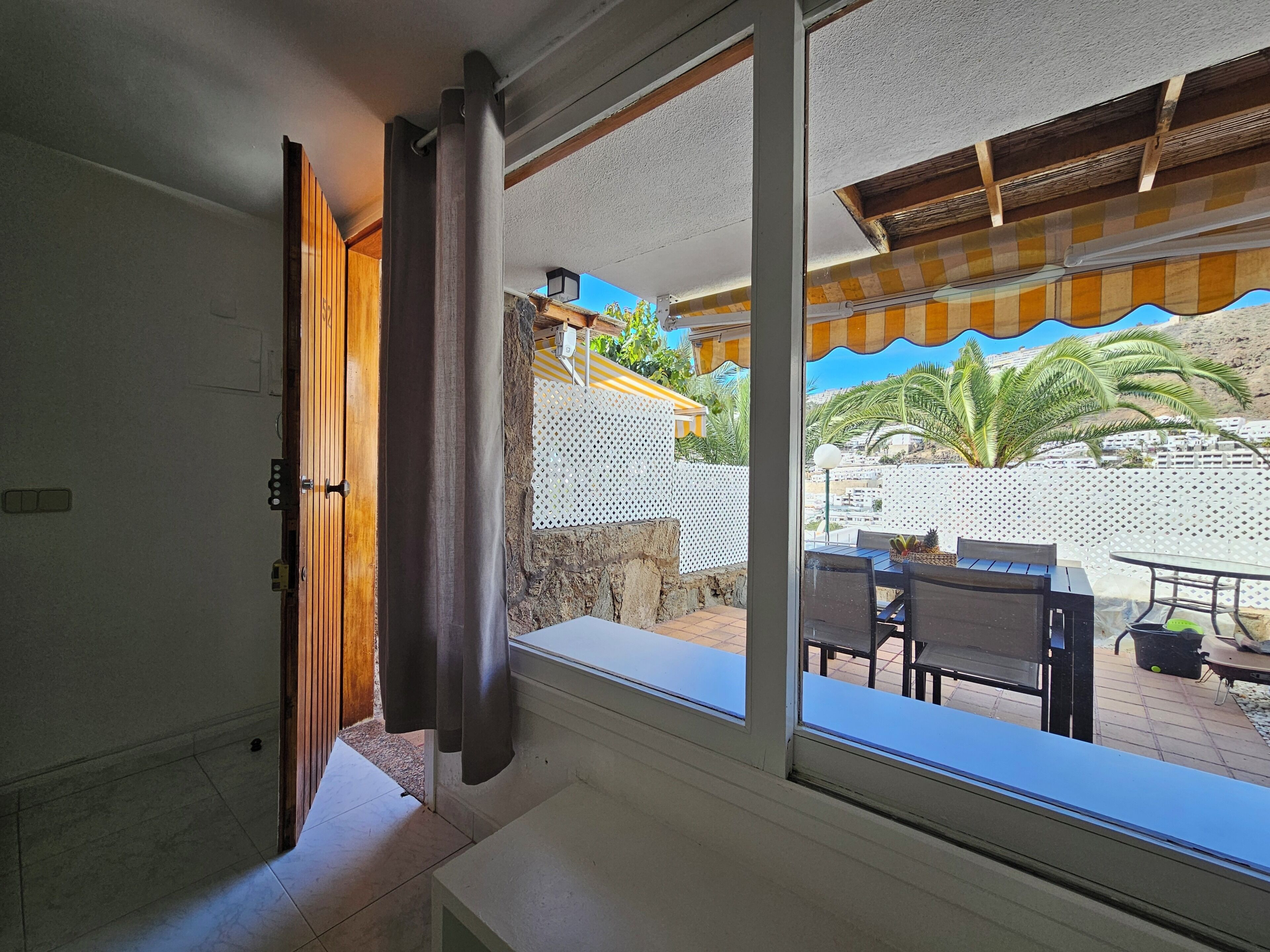 A room with a large window overlooking a patio area with outdoor furniture and a view of palm trees and buildings.