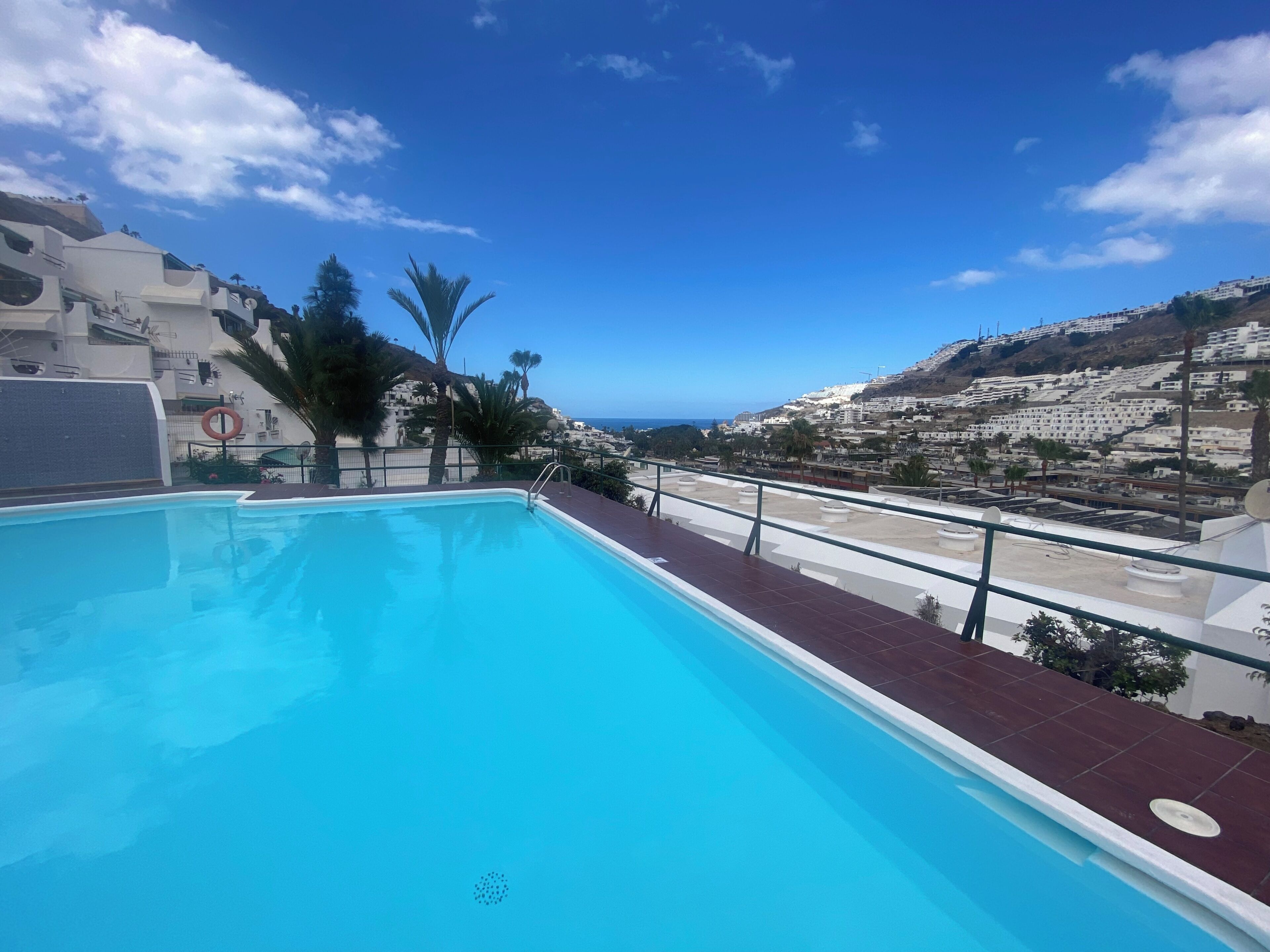 A swimming pool with a view of a coastal town and hills.