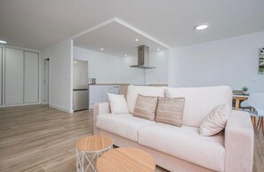 Una sala de estar moderna con un sofá, dos mesas redondas de madera y una cocina al fondo.