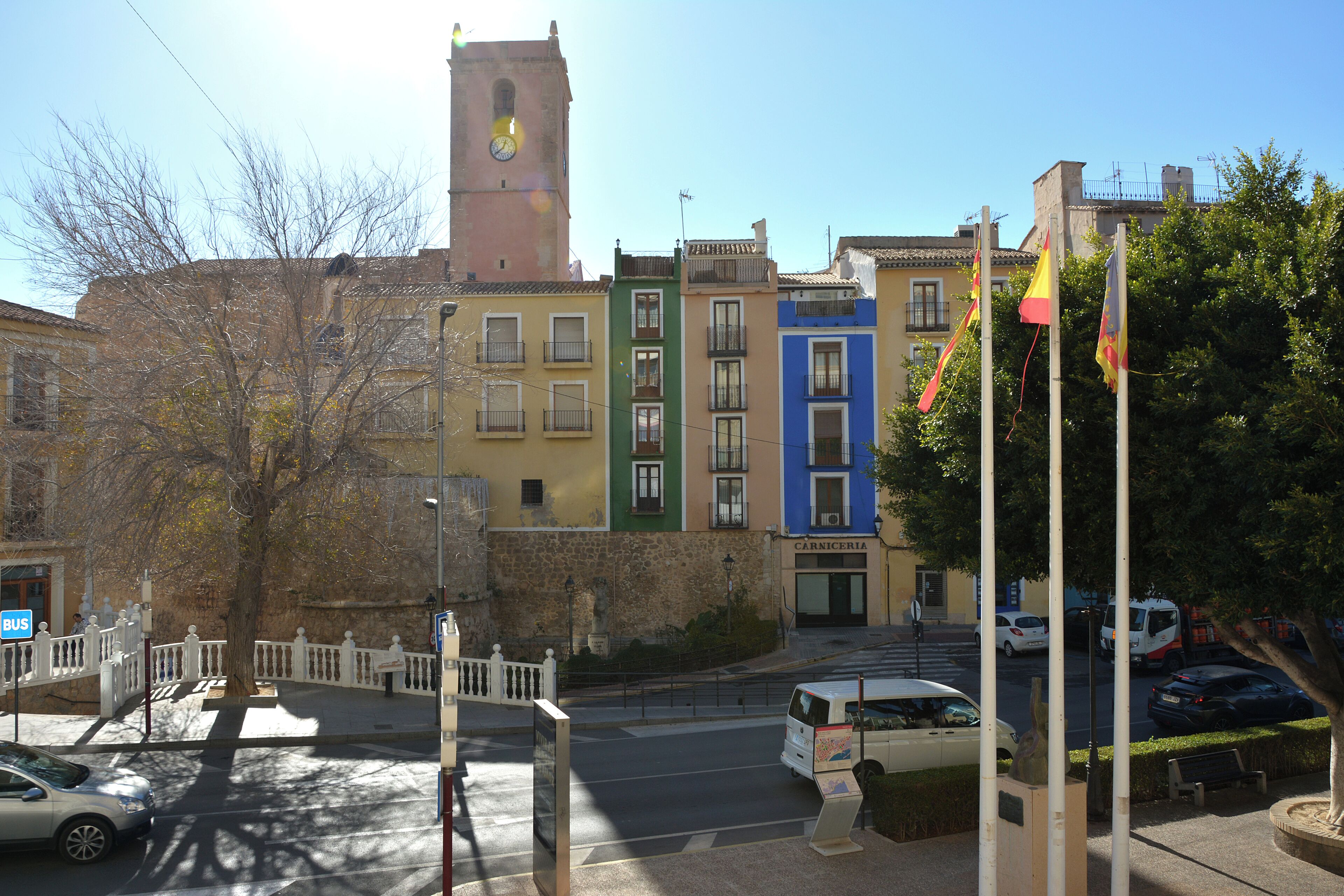 Une vue de rue avec un beffroi, des bâtiments aux couleurs vives et un arrêt de bus.