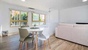 Una sala de estar moderna con un sofá, una mesa de comedor con sillas y ventanas grandes con vistas a espacios verdes.