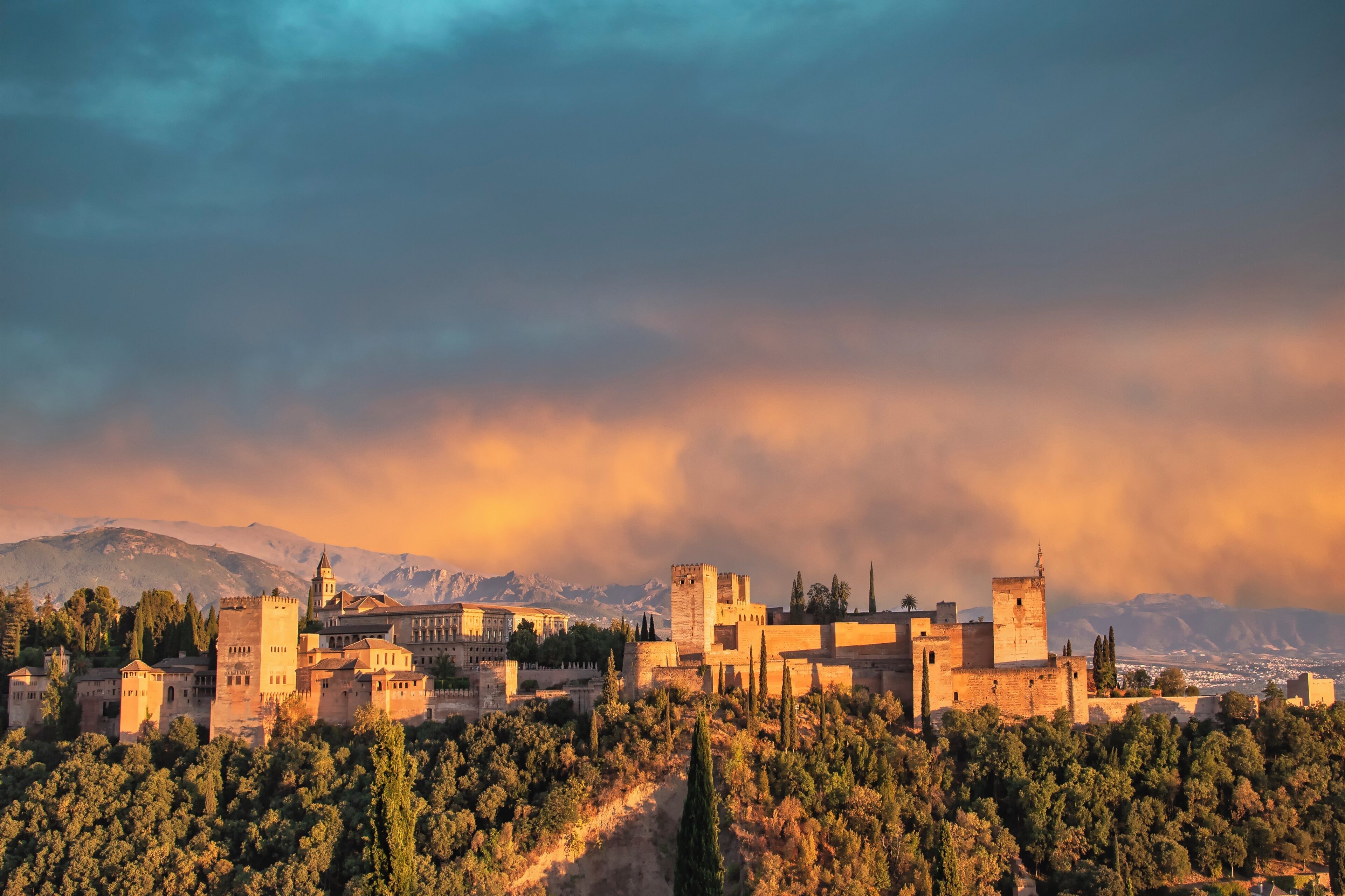 Un complejo de castillos históricos con múltiples torres y fortificaciones, rodeado de abundante vegetación y montañas al fondo.
