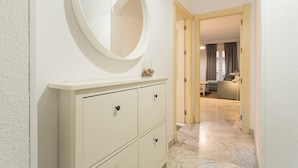 Une salle de bain avec un grand miroir rond, un meuble-lavabo blanc doté de tiroirs et un sol en marbre menant à un espace de vie comprenant un canapé et une lampe.