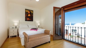 Un dormitorio con cama, mesitas de noche, un banco, ventilador de techo y vistas al exterior.
