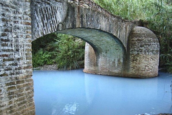 Un pont de pierre enjambant une étendue d’eau calme, entouré de verdure.