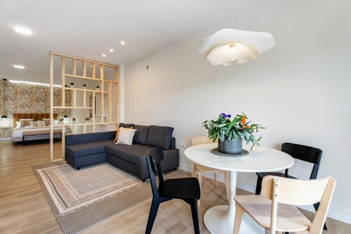 Una sala de estar moderna con un sofá gris, una mesa redonda de comedor con sillas y una lámpara colgante.