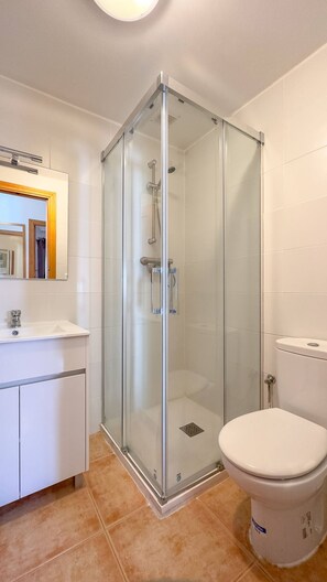 Um banheiro moderno com chuveiro em cabine de vidro, vaso sanitário branco e toucador com espelho.