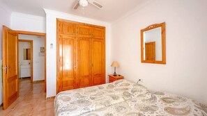 Quarto com cama, guarda-roupa, espelho e mesa de cabeceira com abajur.