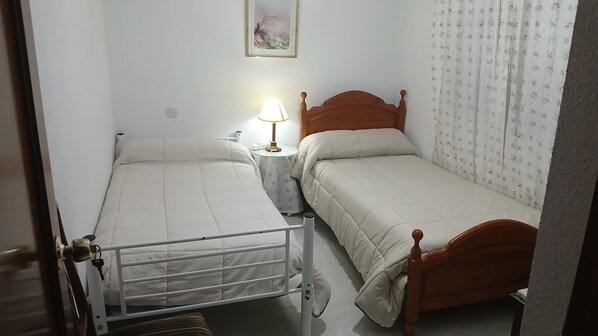 A bedroom with two single beds, a bedside table with a lamp, a wall-mounted painting, and a floral curtain. - Room-habitación Privada Doble Toledo (Toledo)