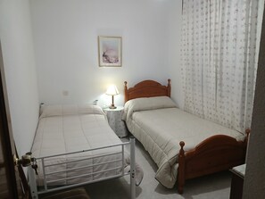 A small, clean room with two single beds, a bedside table with a lamp, a wall-mounted painting, and a curtain with a floral pattern. - Room-habitación Privada Doble Toledo (Toledo)