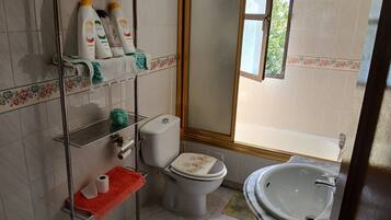 A bathroom with a toilet, sink, and shower area. There are toiletries on a shelf and a towel rack.
