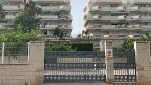 Um edifício residencial com vários andares, varandas, entrada com portão e uma palmeira em primeiro plano.