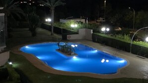 Piscina à noite, com iluminação ao redor e uma pequena fonte.