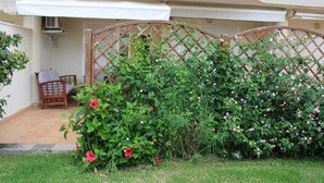 Um jardim com cerca de madeira treliçada, uma cadeira e um pequeno espaço de pátio.