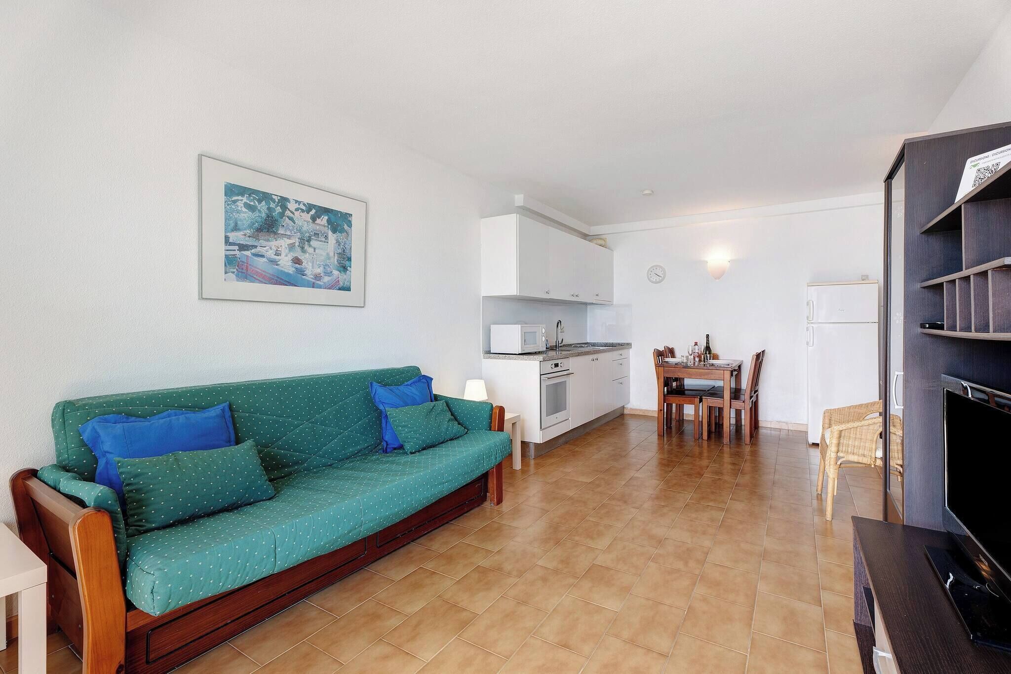 A living room with a sofa, a dining table, a kitchen area, and a TV.