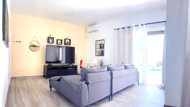 A modern living room with a grey sofa, a flat-screen TV, and a small side table. - Villa Descansa With Private Pool, Air-conditioning, Sea View, Smart-tv & Wifi (Yaiza)