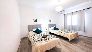 A modern bedroom with two beds, a large window with curtains, and a ceiling light fixture. - Villa Descansa With Private Pool, Air-conditioning, Sea View, Smart-tv & Wifi (Yaiza)