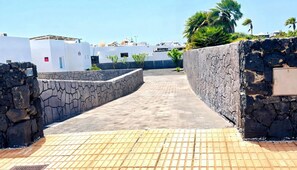 A paved pathway leading to a building with white walls and a stone wall on one side. - Villa Descansa With Private Pool, Air-conditioning, Sea View, Smart-tv & Wifi (Yaiza)