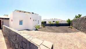 A courtyard with white buildings, a paved area, and a stone wall. - Villa Descansa With Private Pool, Air-conditioning, Sea View, Smart-tv & Wifi (Yaiza)