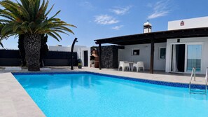A swimming pool with a stone wall and a covered patio area with outdoor seating. - Villa Descansa With Private Pool, Air-conditioning, Sea View, Smart-tv & Wifi (Yaiza)
