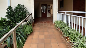 A corridor with tiled flooring, potted plants, a metal railing, and a door leading to an interior space. - Stunning two Bedroom Apartment in Salou (Salou)