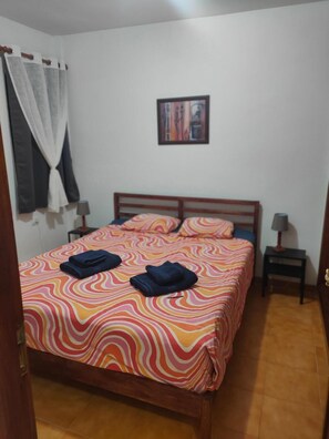 Un dormitorio con cama, dos mesitas de noche, un cuadro en la pared y una ventana con cortinas.