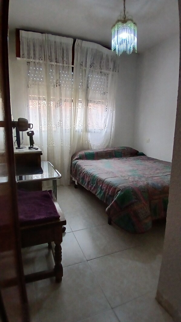 Un dormitorio con una cama, una silla, un escritorio y una lámpara colgante.