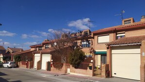 Rua residencial com casas de tijolo, portões de garagem e céu azul claro.