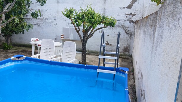 Piscina com cadeiras de plástico branco e uma pequena árvore.