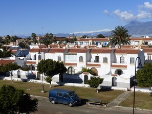 Un quartiere residenziale con edifici bianchi e tetti in tegole rosse, un furgone blu parcheggiato in strada e una palma sullo sfondo.