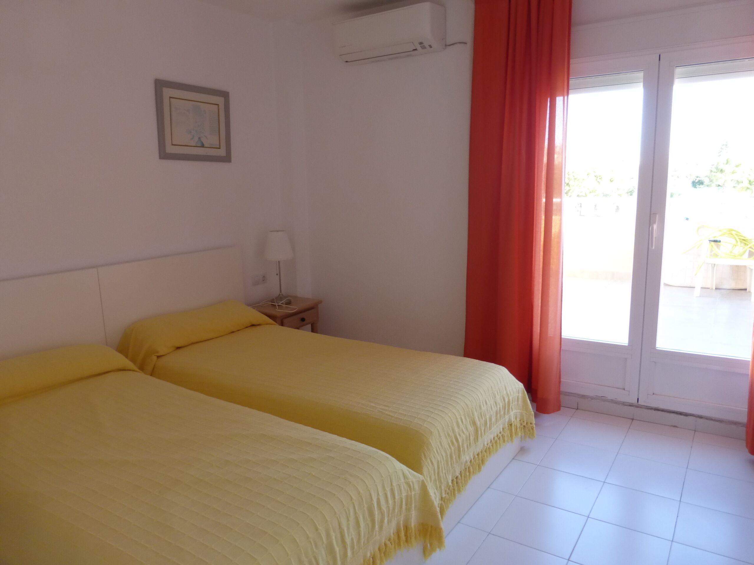A hotel room with two beds, a nightstand, a lamp, a framed picture, and a sliding glass door to the outside.
