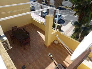 Un balcone con tavolo e sedie, un telescopio e vista su auto parcheggiate e palme.