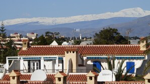 A traditional building with a tiled roof, a white facade, and a blue door. In the background, there is a snow-capped mountain range. - Beautiful 2 Bedroom, 2 Bathroom Apartment (Roquetas de Mar)