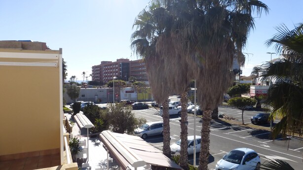A parking lot with several cars, a building with multiple floors, and palm trees. - Beautiful 2 Bedroom, 2 Bathroom Apartment (Roquetas de Mar)