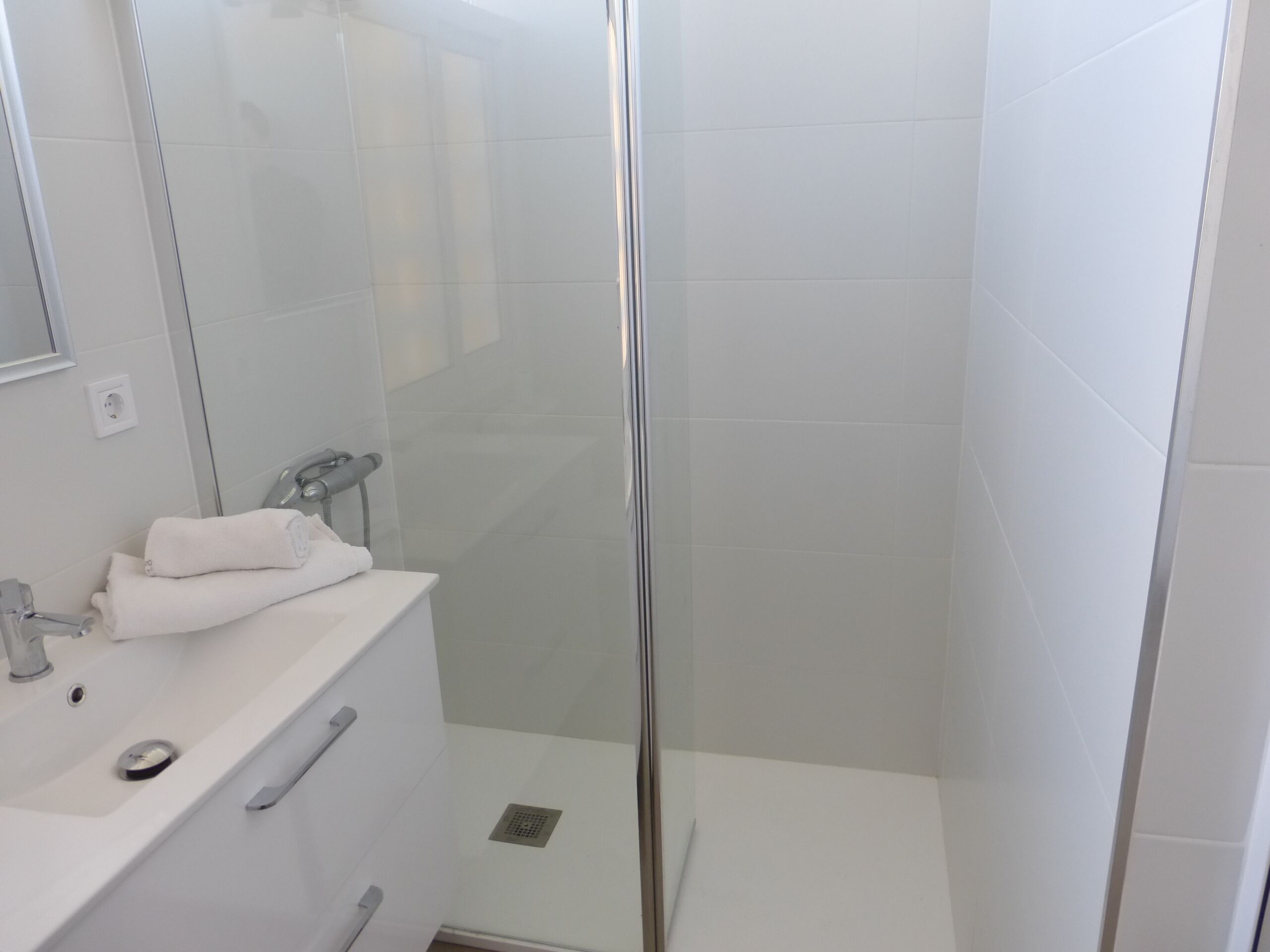 A modern bathroom with a glass shower enclosure, a white sink, and a mirror.
