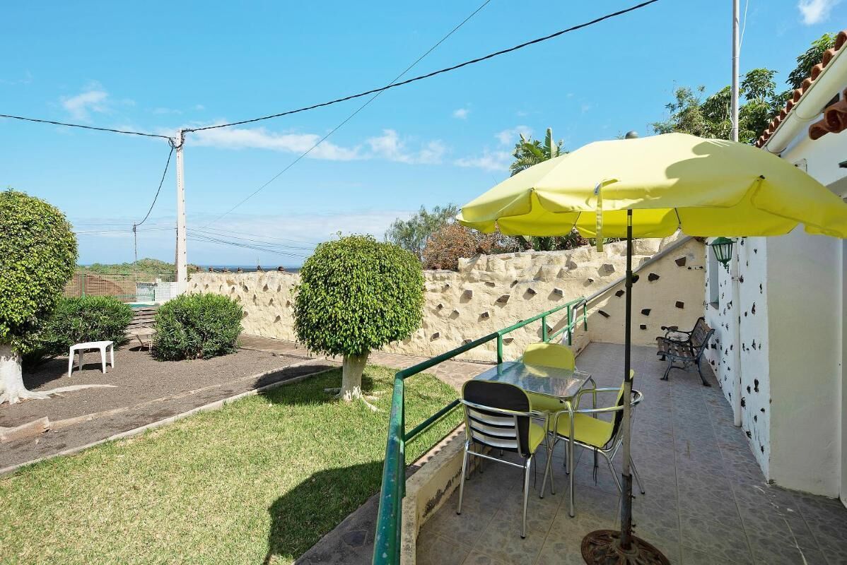 Een terras met een gele parasol, buitenmeubels en een stenen muur.