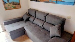 A grey sectional sofa with a footrest and two pillows against a wall with a painting. - House El Cardón A1 in Buenavista del Norte (Buenavista del Norte)